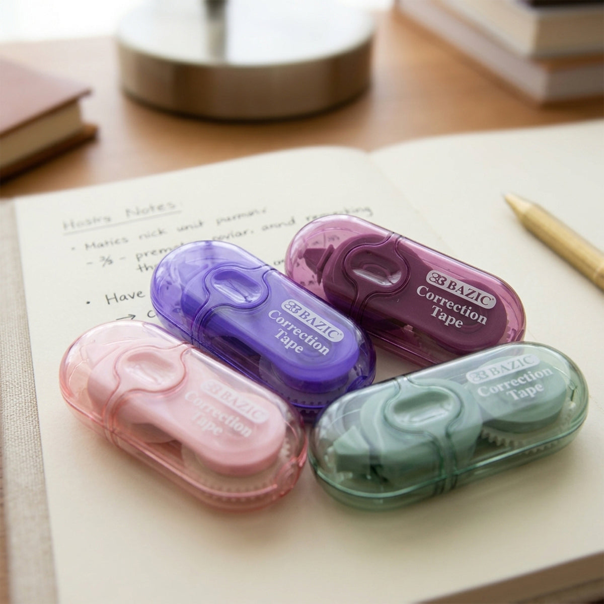 Four mini correction tape dispensers with clear pink, purple, burgundy and mint green cases rest on an open notebook.