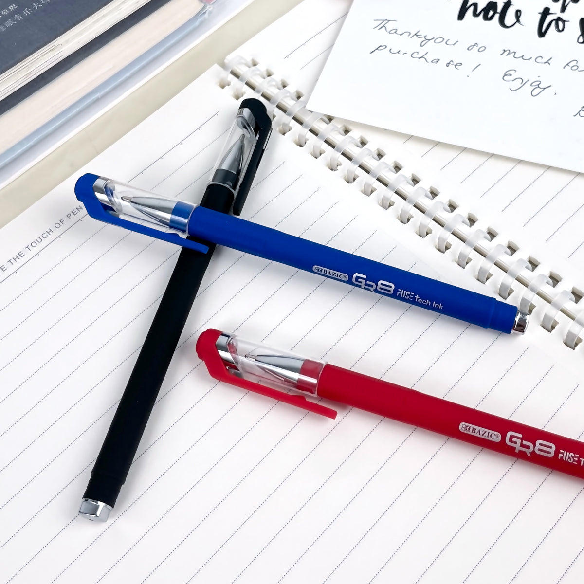 Three capped pens in black, blue and red rest on a lined notebook, with clear caps and matching clips.