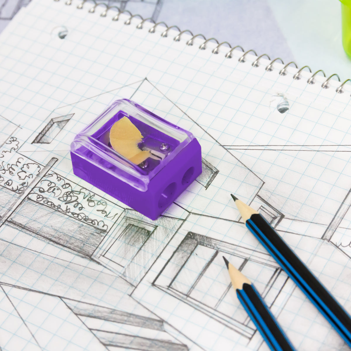 Purple two-hole sharpener with a clear shavings receptacle rests on a sketched notebook beside two sharpened pencils.