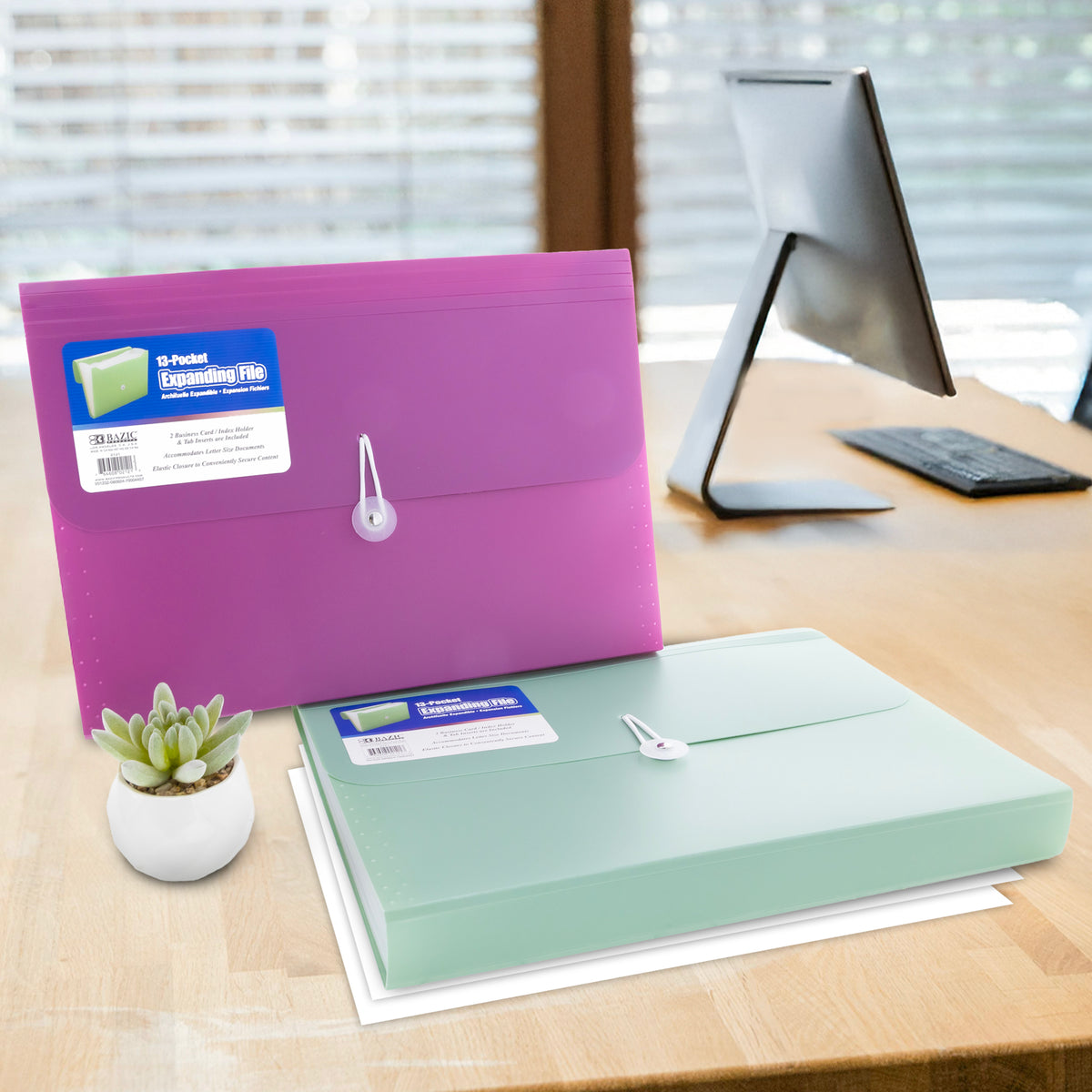 Purple and mint green 13-pocket files with white elastic closures sit on a desk beside a computer.