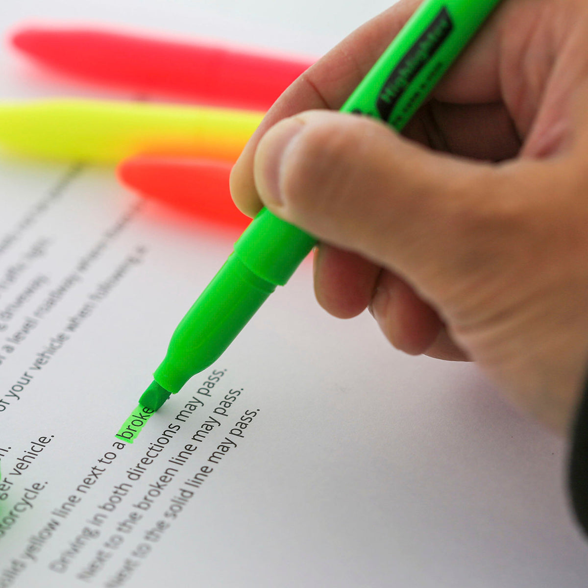 A hand uses a green chisel-tip highlighter to mark printed text on a page.