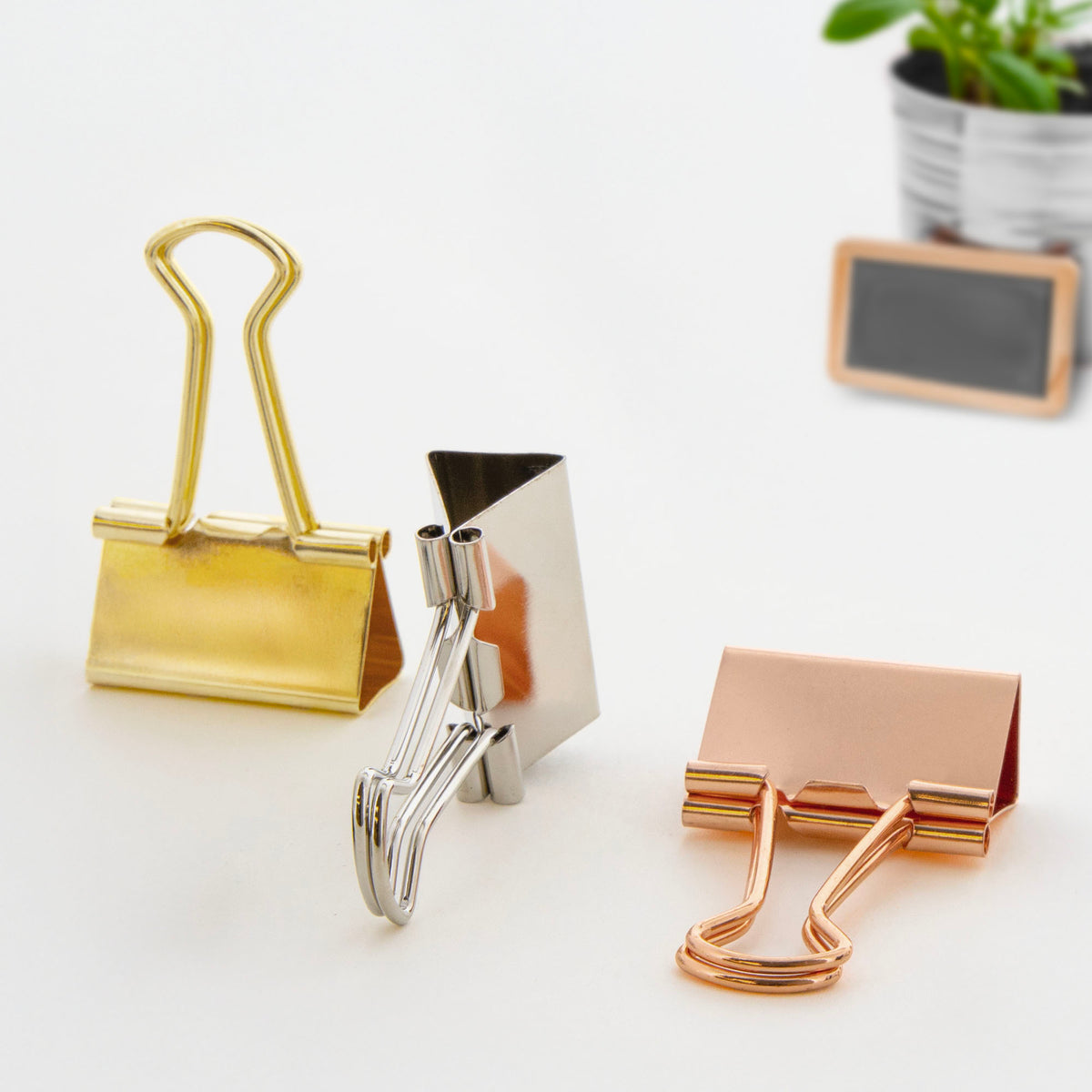 Three metallic binder clips in gold, silver and rose gold, with wire handles shown upright and folded down.