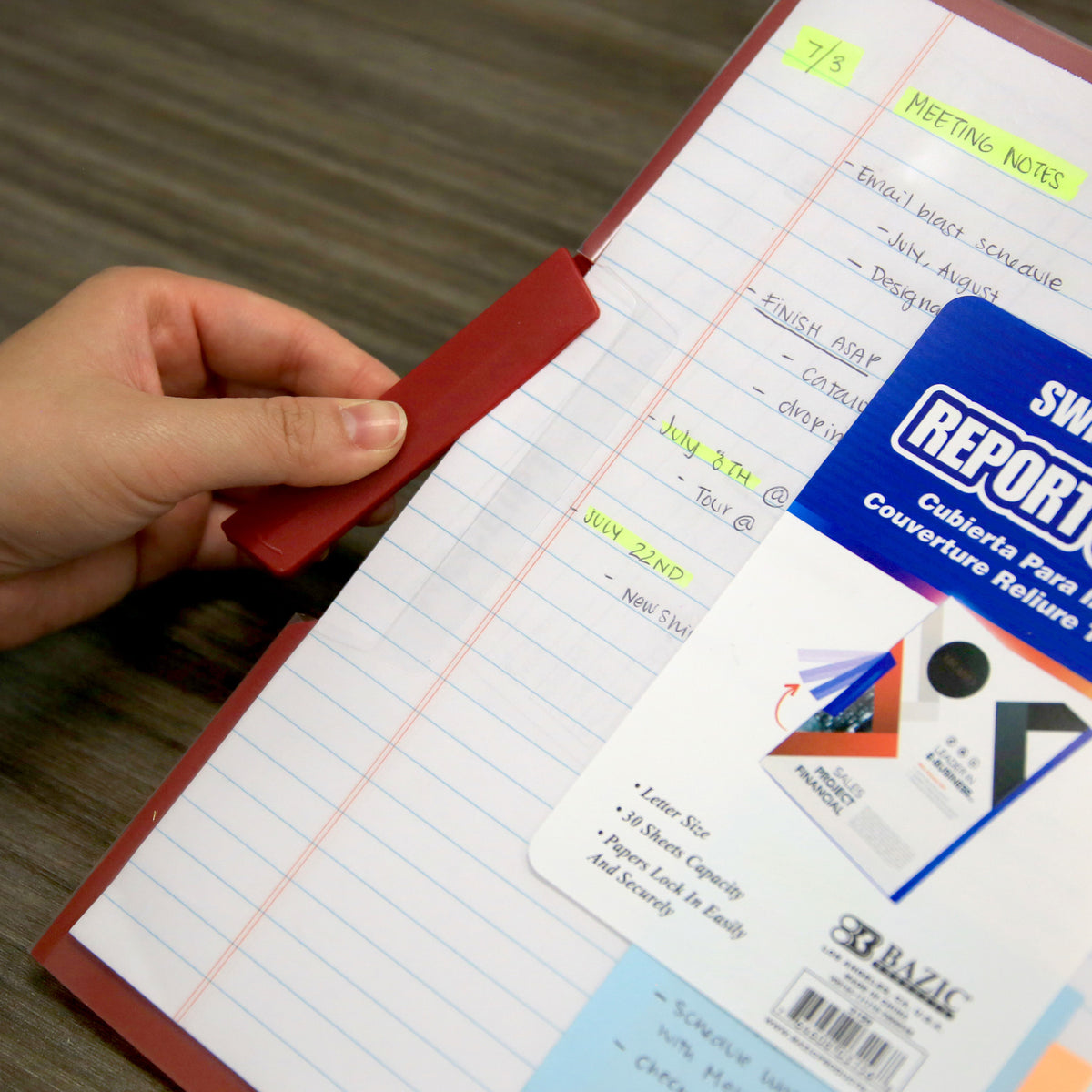 A hand holds open the red swing-lock clip on a clear report cover containing lined meeting notes.