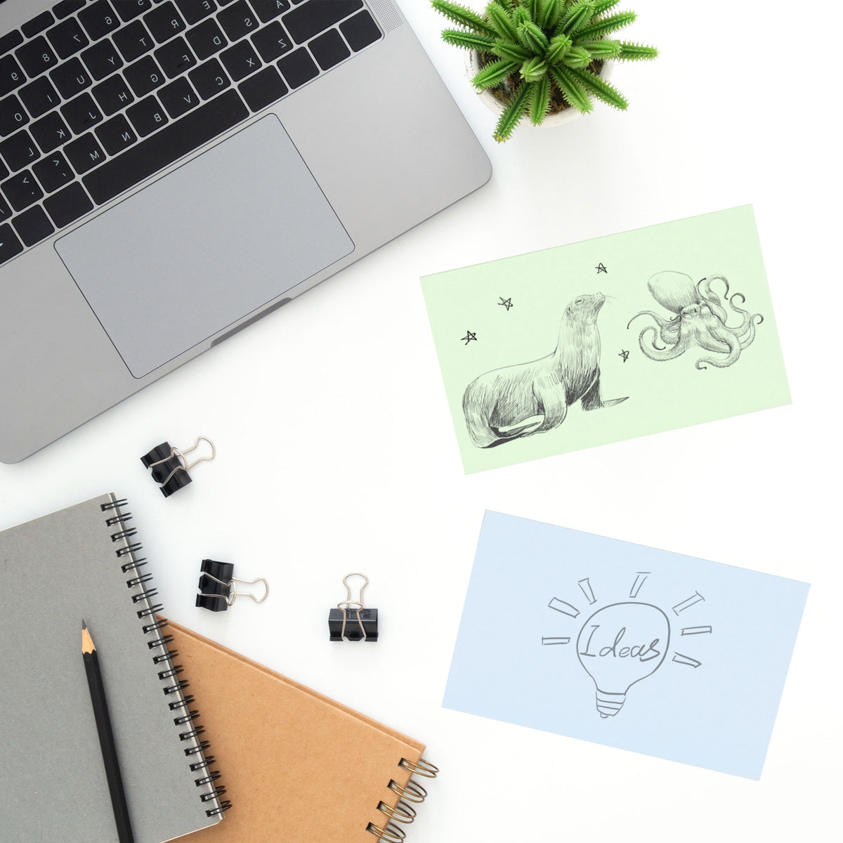Green and blue sticky notes display animal sketches and an Ideas lightbulb drawing on a desk beside a laptop.