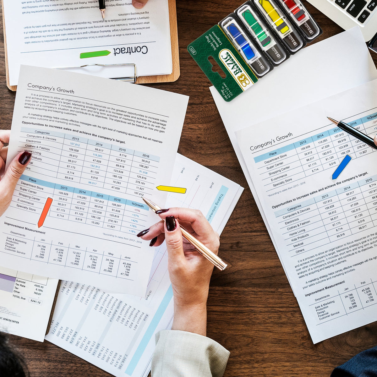 People review business reports marked with neon arrow flags, with four flag dispensers on the desk.