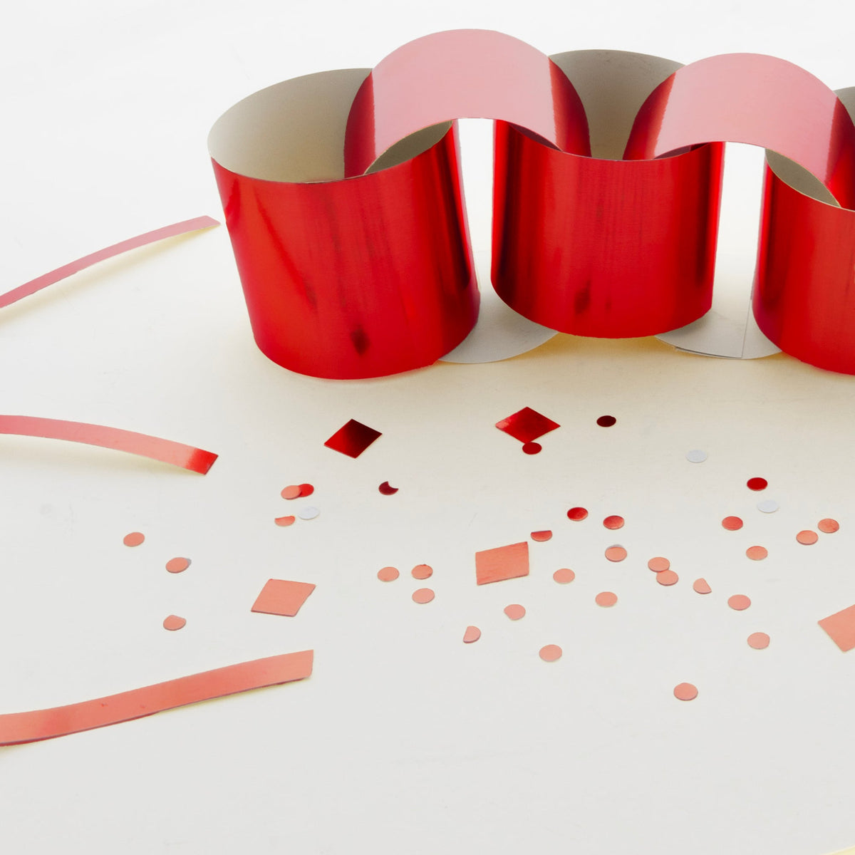 Shiny red poster board curled into loops, with beige backing visible and small circle, square and strip cutouts nearby.