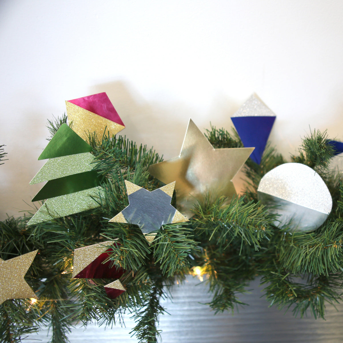 Gold and silver stars and colorful geometric cutouts decorate an evergreen garland with string lights.