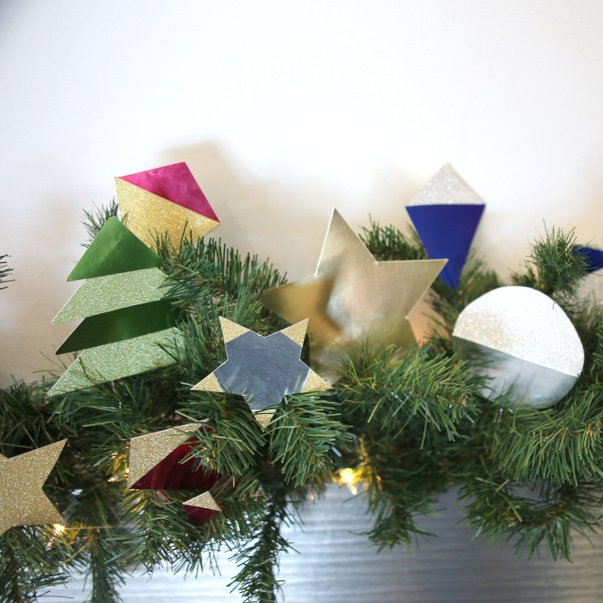 Metallic silver and colorful board cutouts shaped as stars, circles and folded ornaments decorate a pine garland.