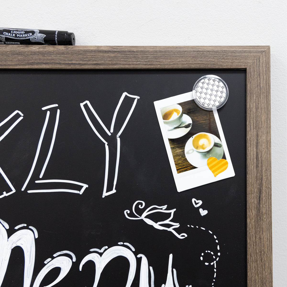 Close-up of brown wood frame and black chalkboard with white lettering and a round magnet holding a coffee photo.