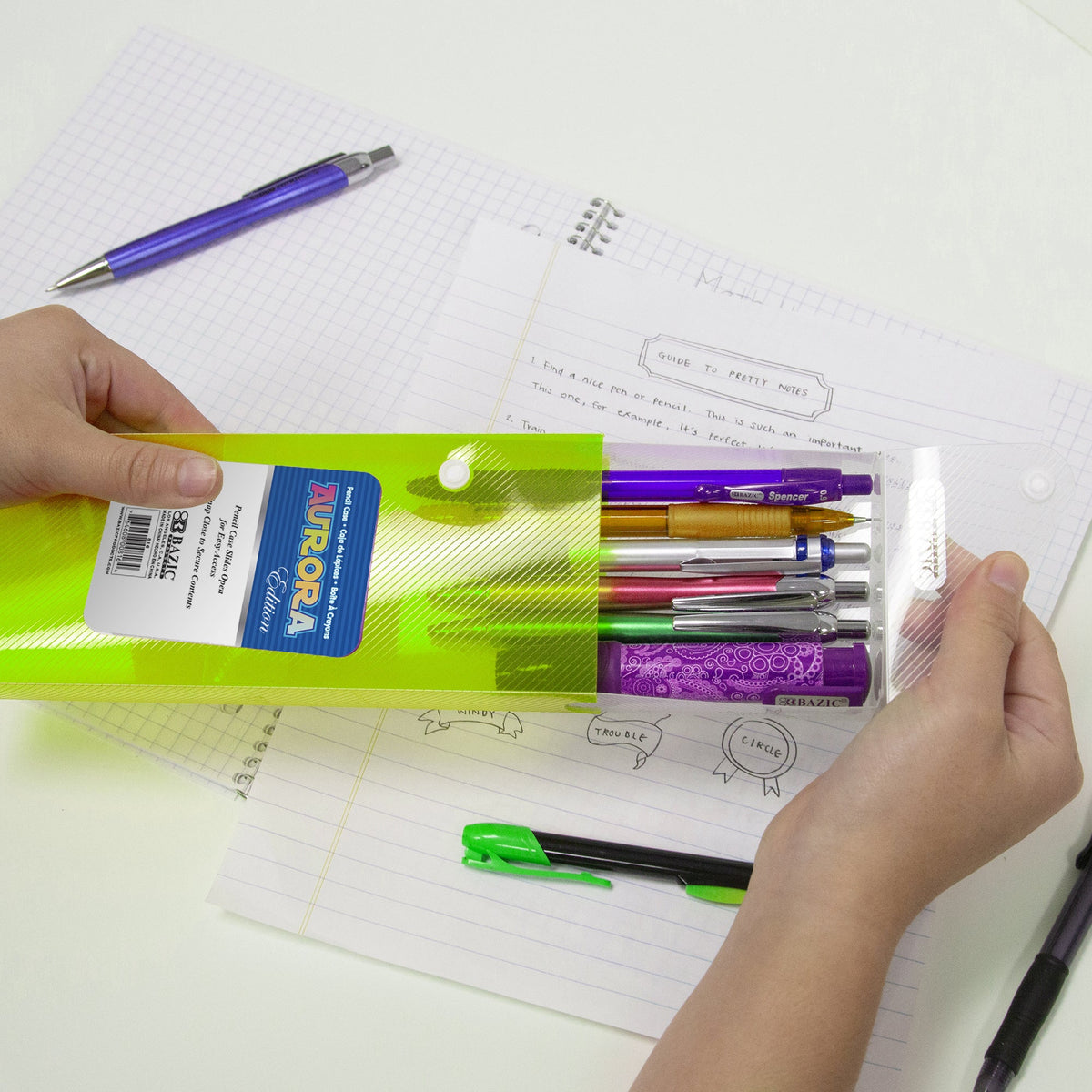 A person slides open a translucent lime green pencil case filled with colorful pens over an open notebook.