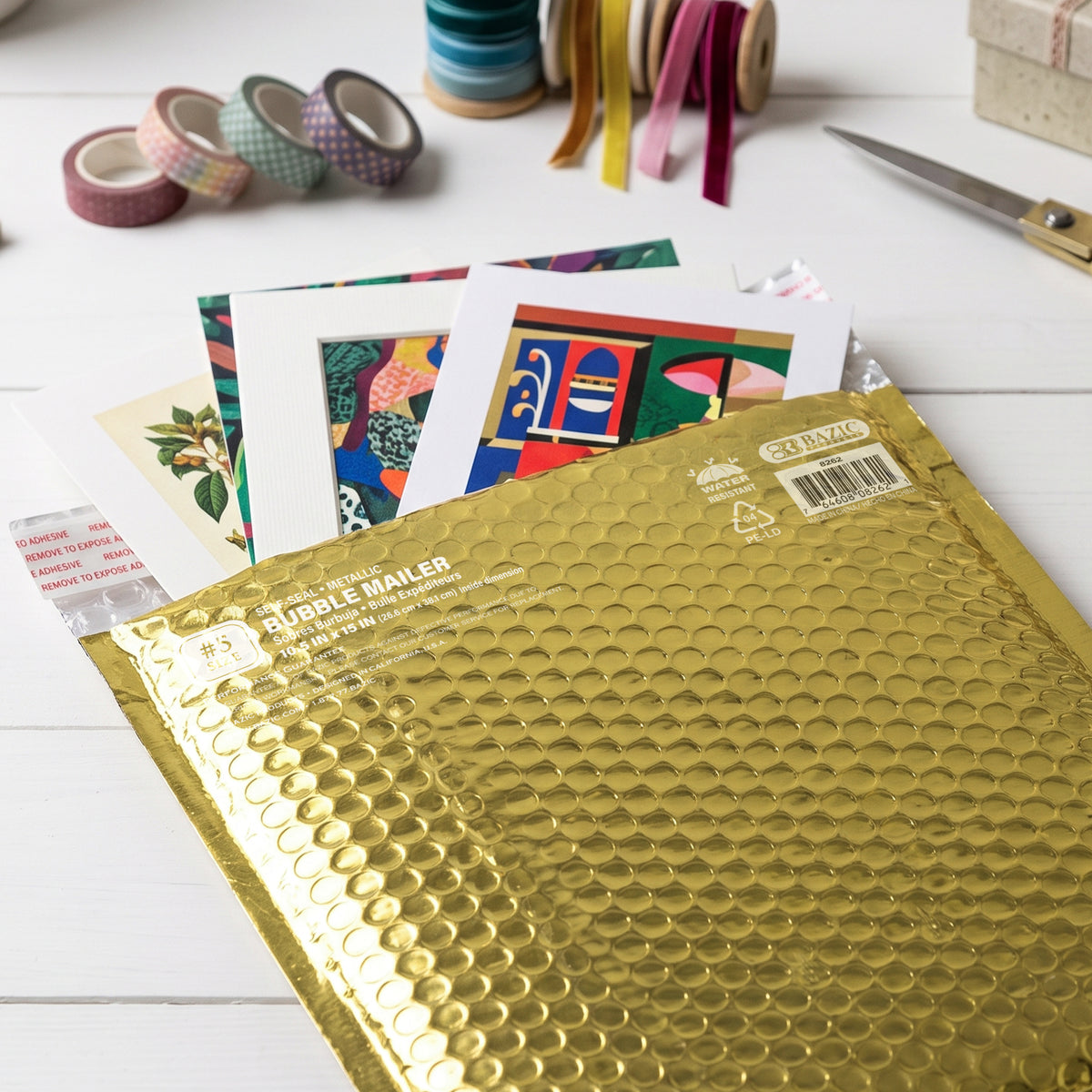 Gold bubble mailer holds art prints on a craft table; labeled self-seal, water resistant, 10.5 x 15 in.
