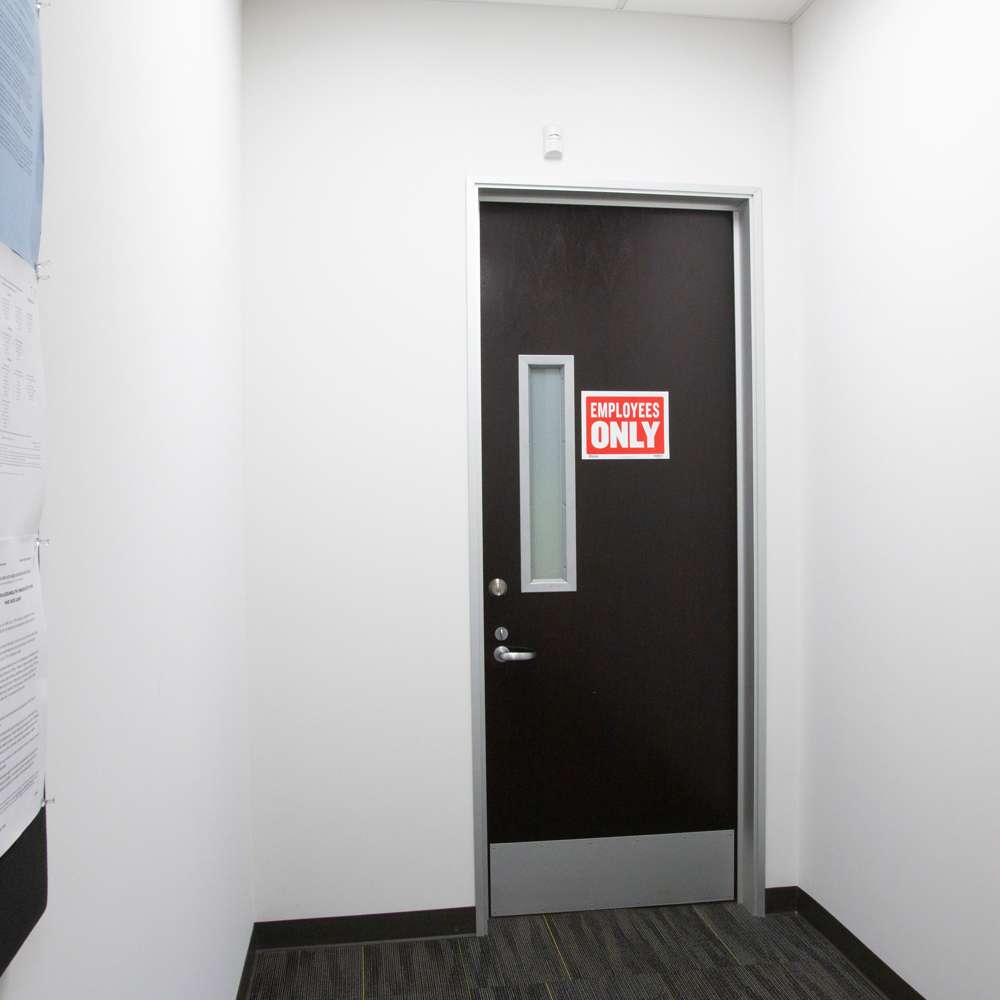 Red and white Employees Only sign mounted on a dark office door beside a narrow window.