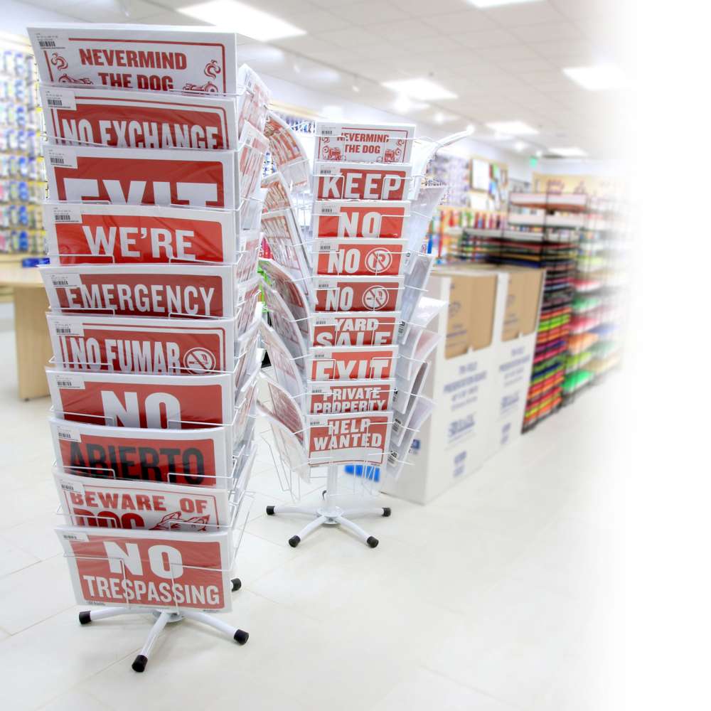 Store display racks hold red and white signs, including No fumar, Abierto, Exit, Yard sale and Help wanted.
